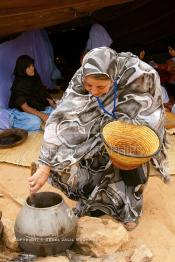 Image du Maroc Professionnelle de  Sous une tente bédouine plusieurs femmes du Sahara  préparent le couscous durant le grand Moussem de Tan Tan, classé en 2005 patrimoine immatériel humain mondial de l'Unesco. Le Moussem est une sorte de foire annuelle, à la fois économique, culturelle et sociale. Chaque année la majorité des tribus et des grandes familles nomades du désert se retrouvent sur un site désertique "Place de la Tolérance et de la Paix " à la périphérie de Tan Tan où  danse, chants, course de chameaux et fantasia font partie des festivités. , Samedi 18 septembre 2004, ((Photo / Abdeljalil Bounhar)